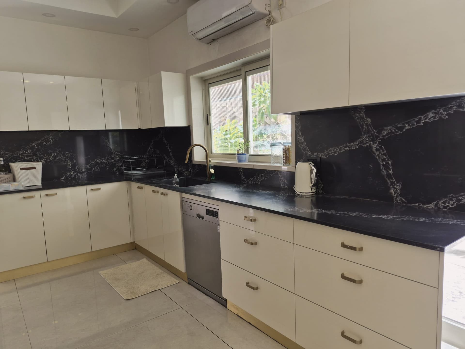 מטבח מודרני מרווח עם ארונות לבנים, משטח שיש שחור וחלון גדול, וילה אילת.