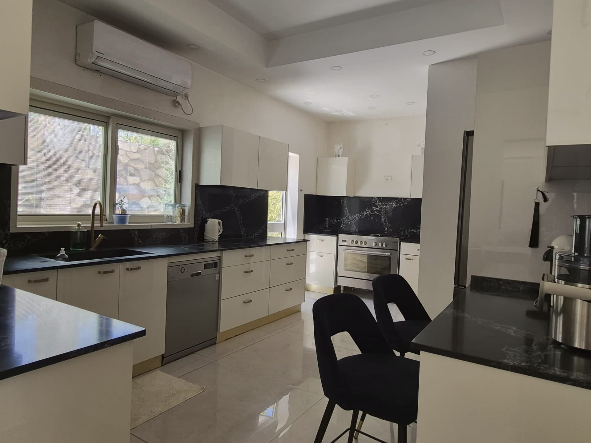 מטבח מודרני מואר עם משטחי שיש שחורים, כיור, מדיח, תנור ואי ישיבה. וילה באילת.