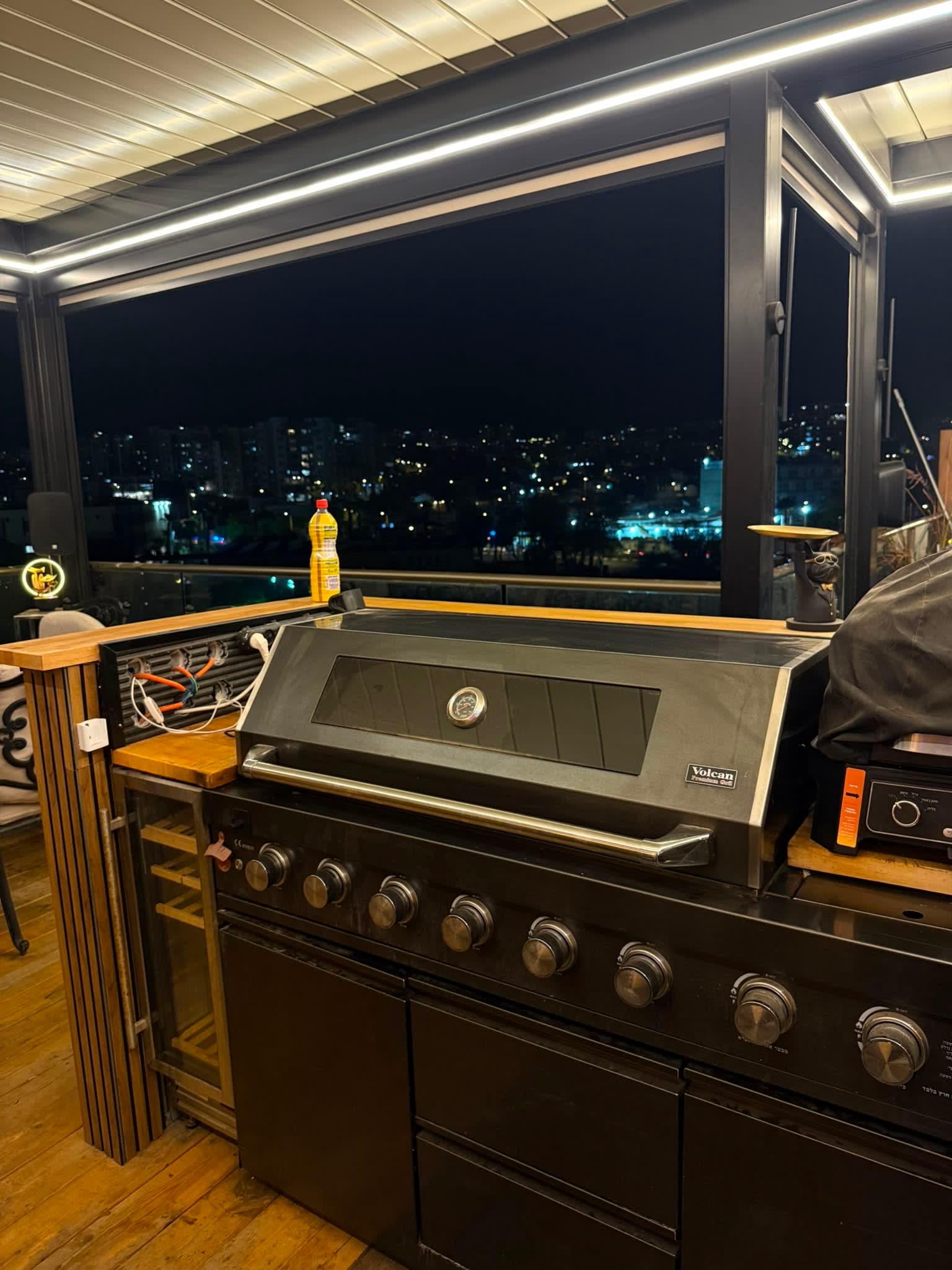 מרפסת גג עם גריל גז יוקרתי ותאורת לד, נוף עירוני לילי אילת.