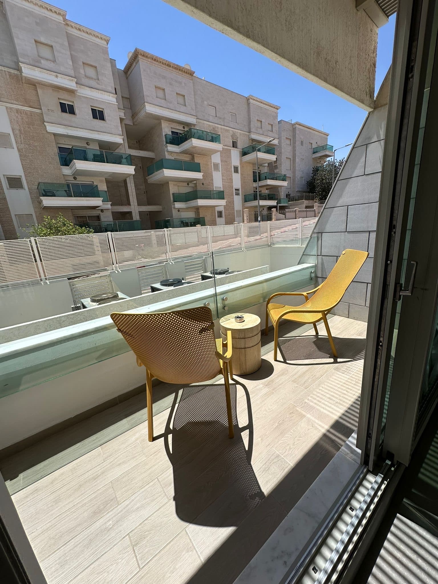 מרפסת שמש עם שני כיסאות צהובים ושולחן צד קטן, דירת נופש אילת.